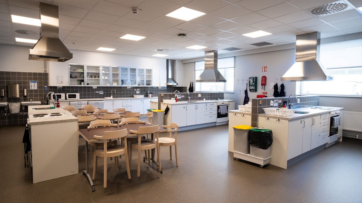 En rymlig matstudio med flera köksstationer, spisar, arbetsbänkar och matbord placerade i mitten av rummet.