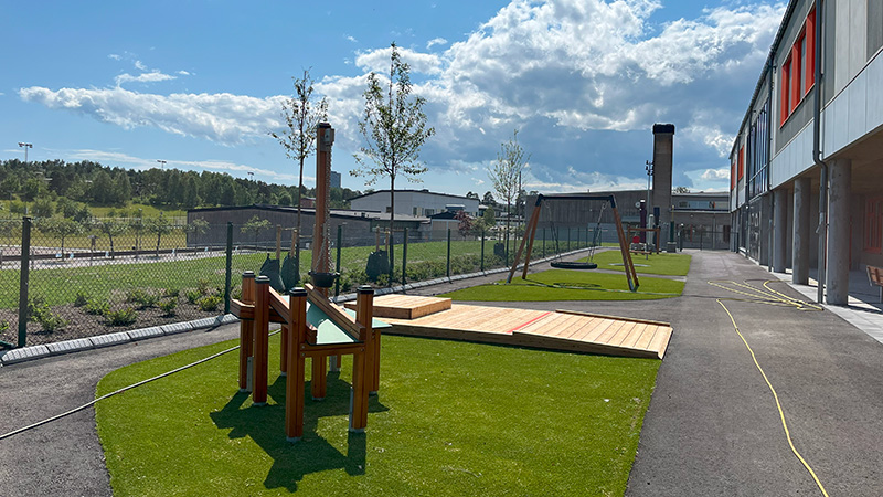 Skolgård med gångar av asfalt. En gräsmatta med aktivitetstationer i trä.