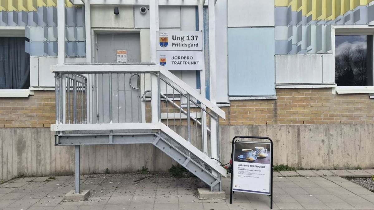 Entré med trappa till Träffpunkt Jordbro. Utanför står ett gatupratarställ med information om verksamheten.
