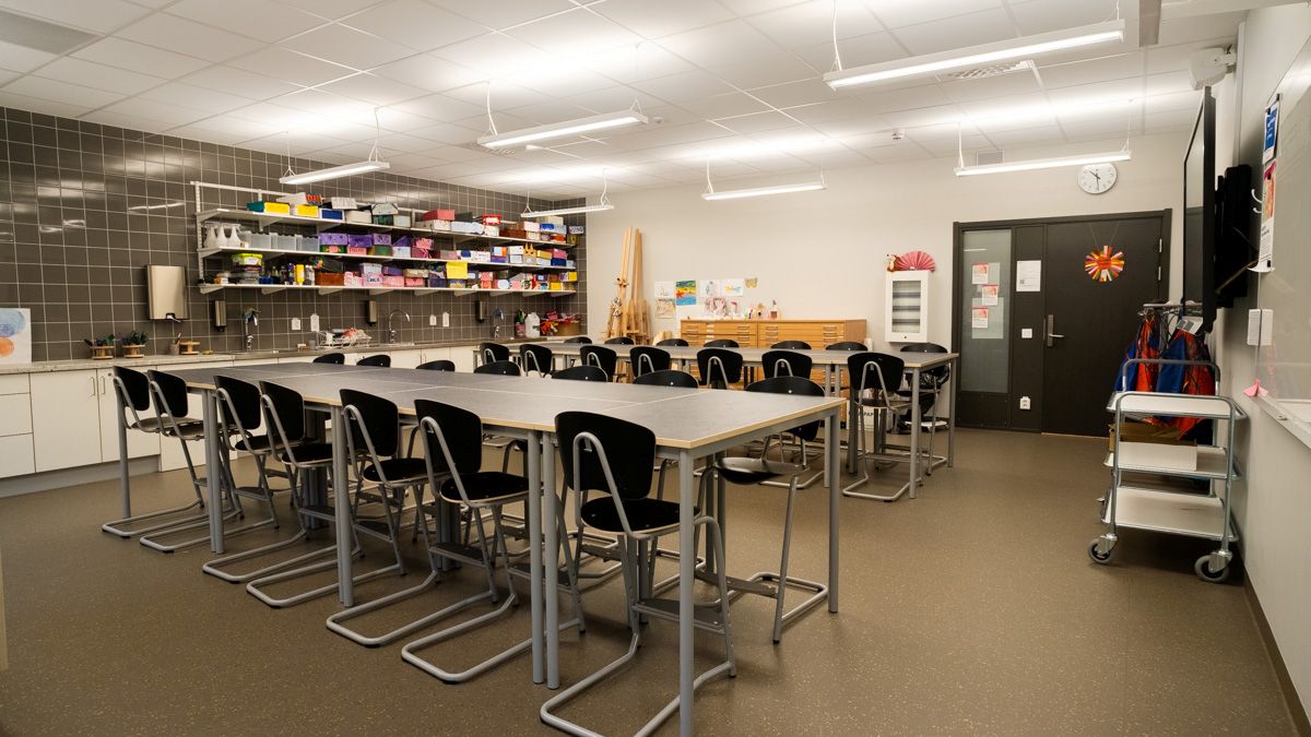 En bildsal med höga bord och pallar, hyllor fyllda med material och redskap längs väggen samt arbetsytor för skapande.