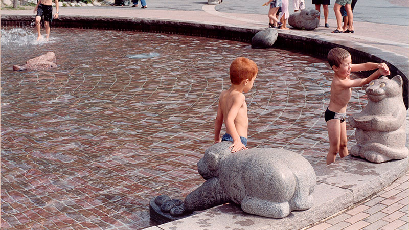 Två barn leker i plaskdammen med stenstatyerna En fågel i handen