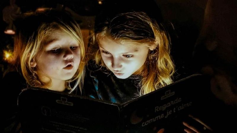 Bild på två barn som läser en bok i ett mörkt rum