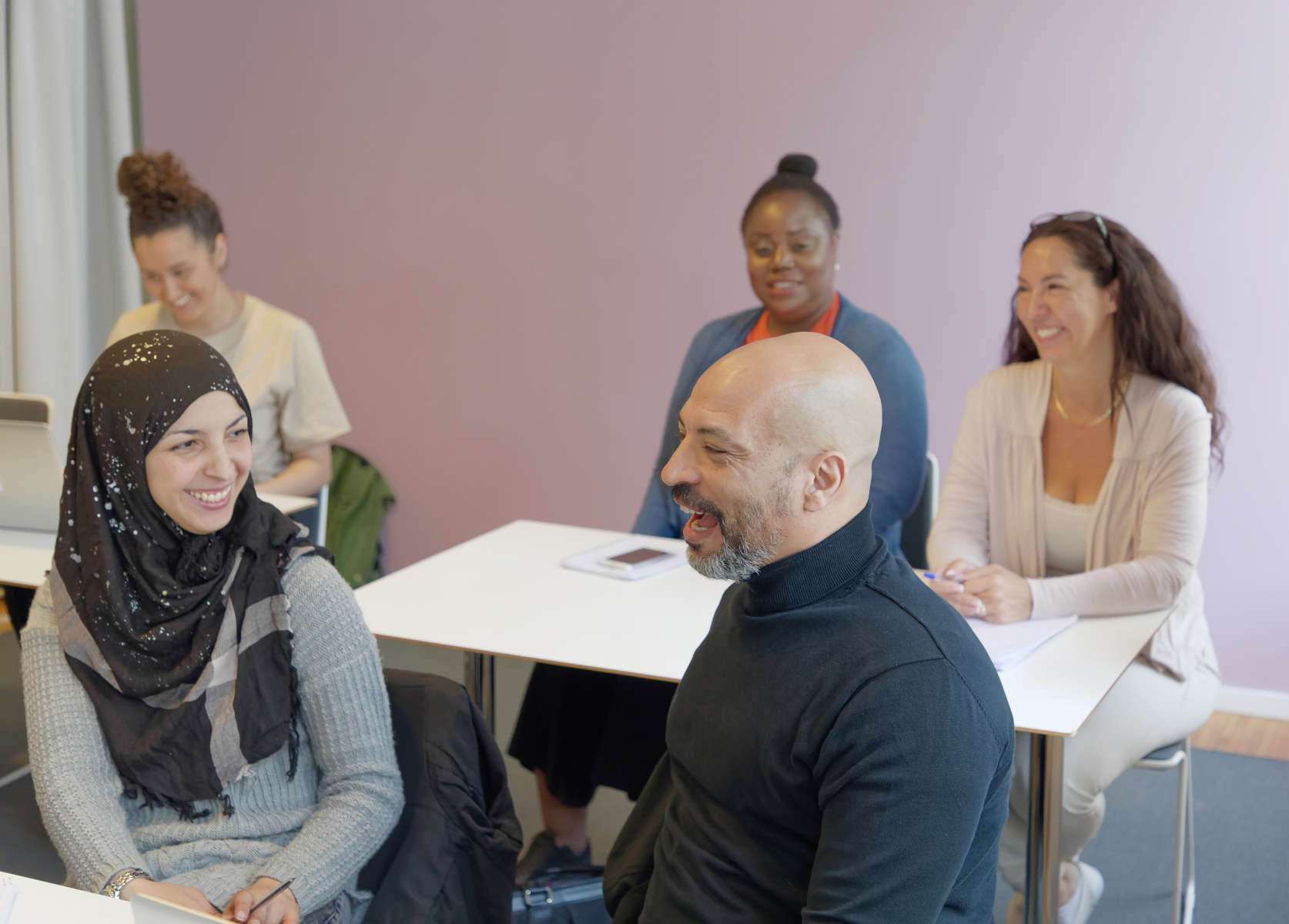 En grupp på fem vuxna studenter sitter i ett klassrum och pratar med varandra.