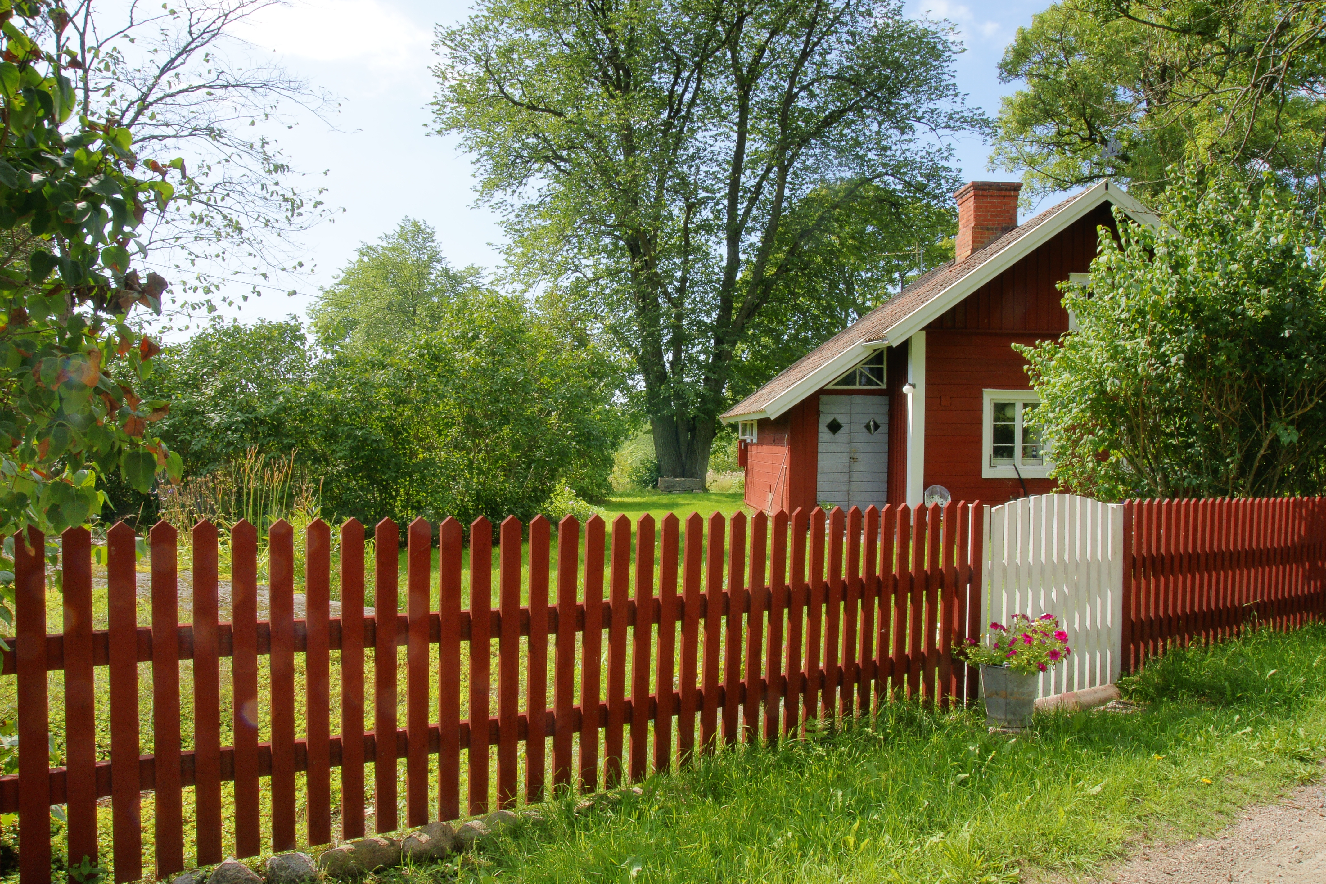 Rött staket, vit grind och liten röd stuga.