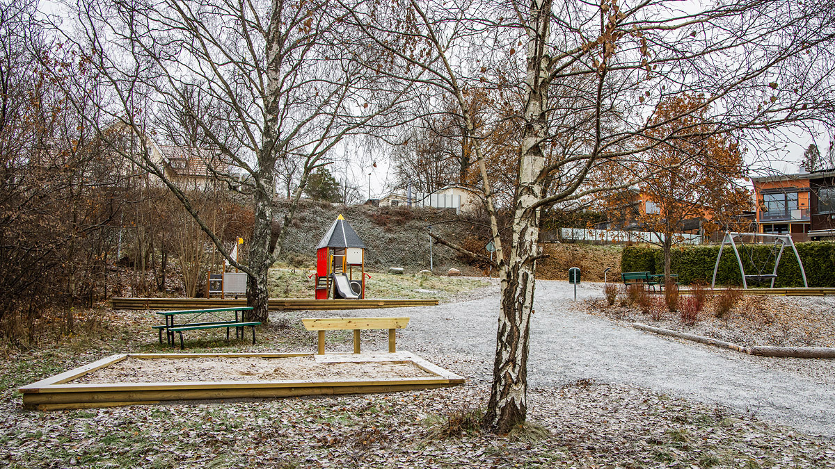 Lekhus, gunga och sandlåda omgiven av björkar