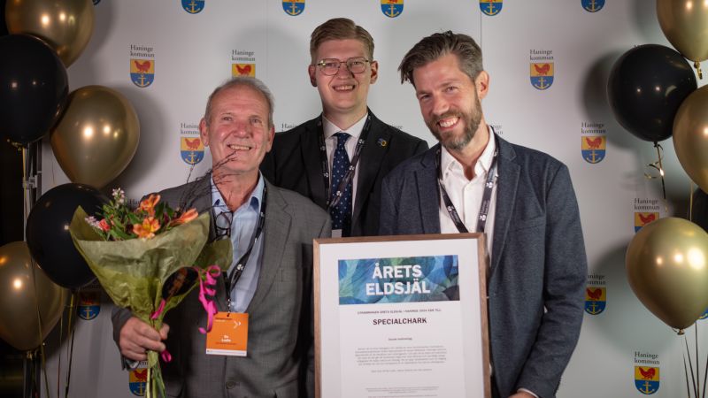 Två  män håller diplom för årets eldsjäl. IAdam Simonsson i mitten., framflr vägg med Haningeemblem och ballonger. 