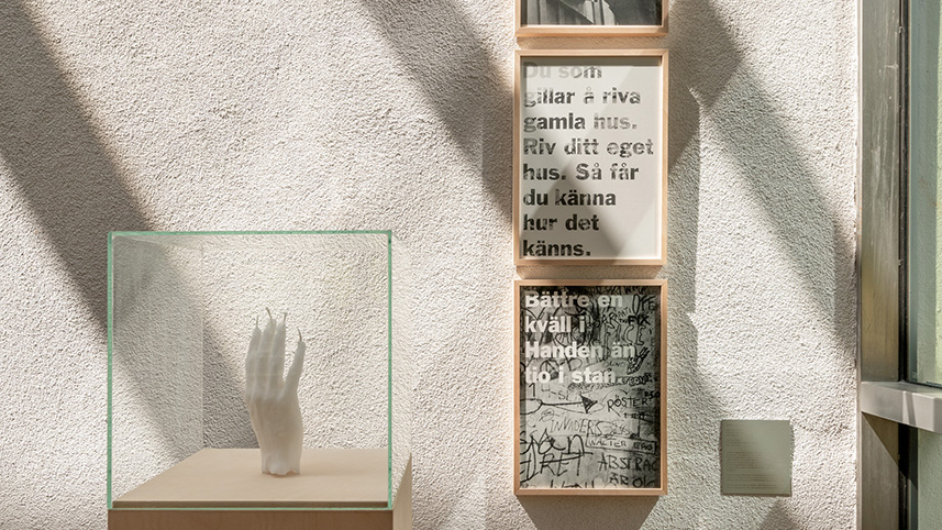 Skulptur av en hand och tre texter uppsatta på väggen.