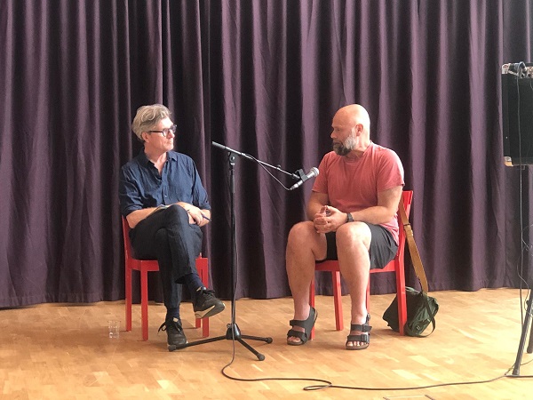 Två män samtalar på en scen.